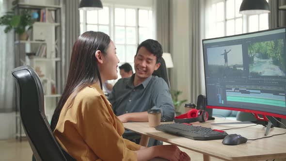 Happy Asian Female Video And Sound Editor Works With Her Male Colleague On Personal Computer