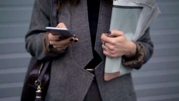 Pan Shot of Woman Holding Newspapers and Typing in the Phone