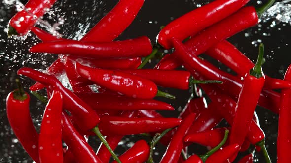 Super Slow Motion Shot of Flying Fresh Chilli Peppers and Water Side Splash on Black at 1000 Fps