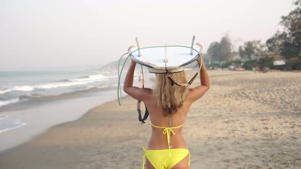 Young Sexy Woman Surfer in Bikini Carries a Surfboard on Her Head Along the Beach