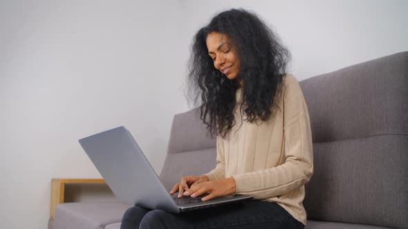 Smiling black woman typing on notebook computer keyboard in living room