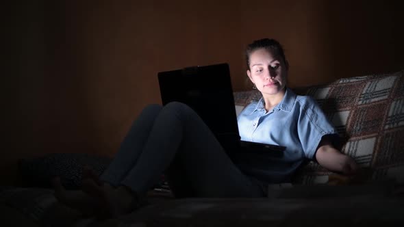 Girl works at the laptop late at home and eats pizza on a sofa