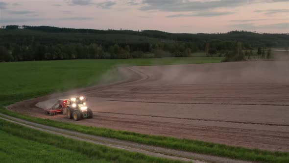 AERIAL, sowing pea and oat seeds at dusk in a dusty field, Sweden