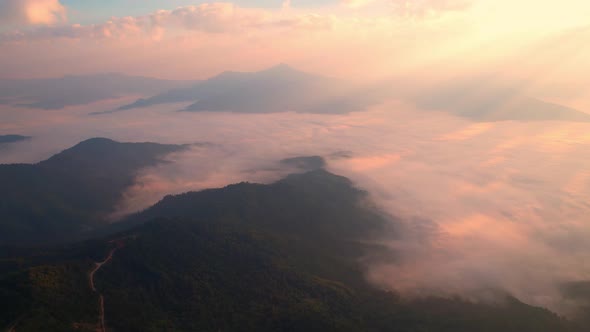 The rays of the sun shine through the clouds into the misty above the mountains in the morning