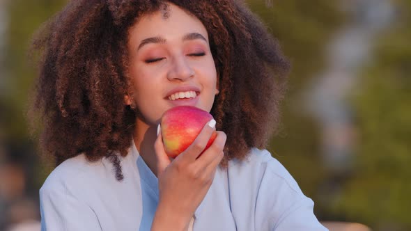 Afro American Woman African Curly Girl Sitting Outdoors Sniffs Red Fresh Ripe Apple Delicious Fruit