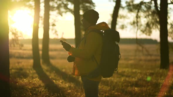 Man Hiker Backpacker Traveler Camper with Her Phone Looks at a Map or Route Under Sun Light