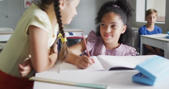 Video of happy diverse girls at desk doing lessons together in classroom