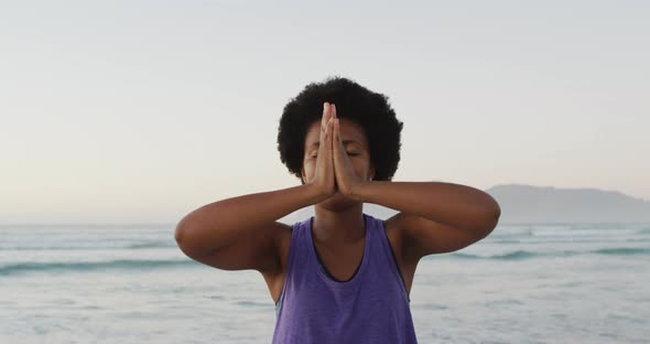 African american woman practicing yoga and meditating on sunny beach