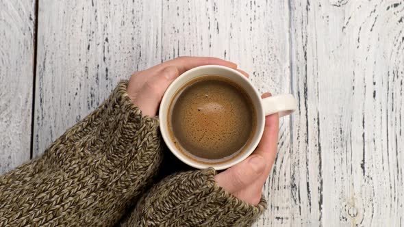 Female Hands Holding Cup of Hot Coffee on Old White Wooden Background, Coffee Foam Swirls in White