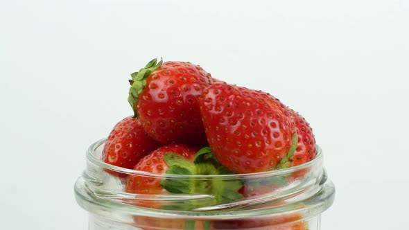 Glass jar with red ripe strawberries rotating on a white background. Ripe summer red strawberry