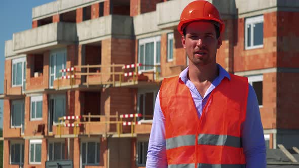 Construction Worker Talks To Camera in Front of Building Site