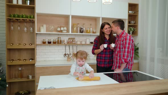 Little Girl Rolls Dough while her Parents Drink Coffee in Kitchen