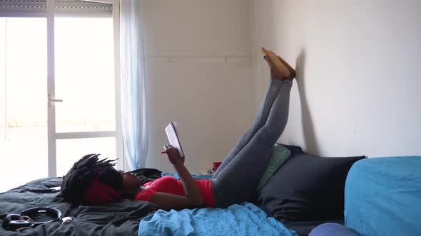 Young woman writing notes in notebook lying on bed
