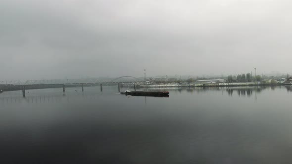 Big scow is sailing on river through smog among industrial city center.