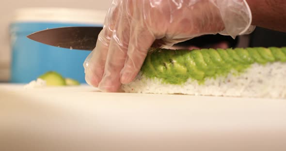 Hands With Disposable Plastic Gloves Carefully Slicing Sushi Rolls With Avocado And fried Tempura Us