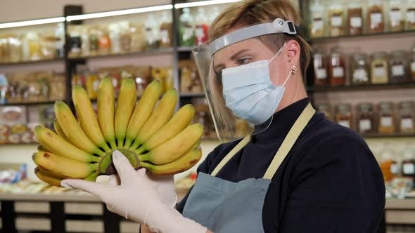 Closeup of a Salesman in a Mask Holding Small Bananas in a Grocery Store