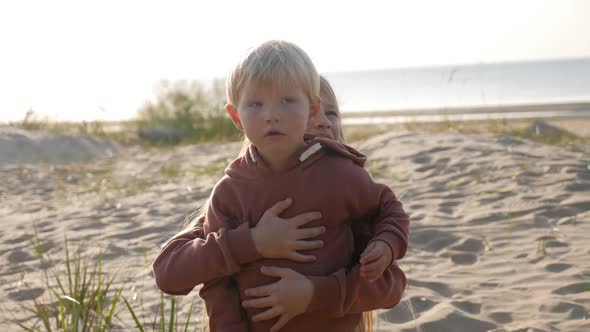 Brother and Sister in a Hoodie Sit on the Sand