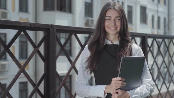 Portrait of a Pretty Young Woman on the Terrace Looking in the Camera Holding Laptop in Hands