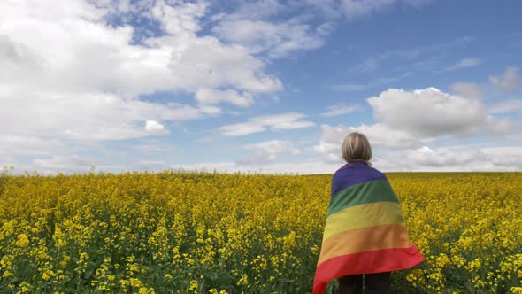 Female with LGBT rainbow flag on yellow rapeseed field in spring