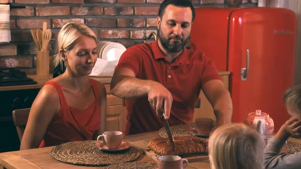 A Happy Family Is Sitting at a Table in the Kitchen on a Cozy Evening, Father Cuts the Cake That Mom