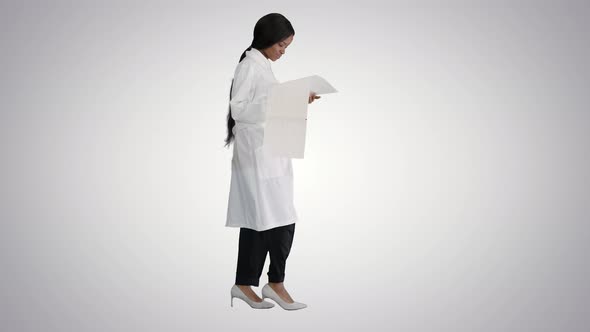 Afro American Doctor Woman Walking and Looking at Cardiogram Record on Gradient Background.