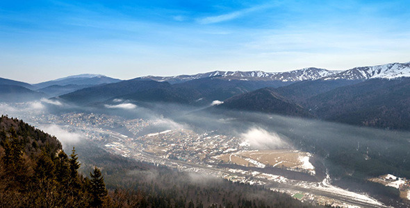 City Between Mountains With Cloudy Sky And Fog