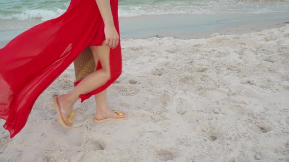 slow-motion of woman feet in red dress walking on the sea beach with wind blow