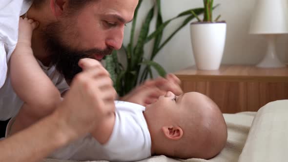 Authentic Bearded Longhaired Young Neo Father And Newborn Baby Looking Each Other Smiling On Bed