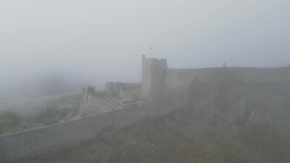 A drone rotates around a flag on the Castle of Marvão in thick mist.