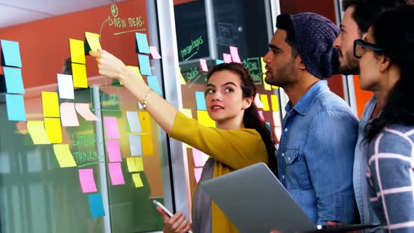 Smiling executives discussing over sticky notes on glass wall