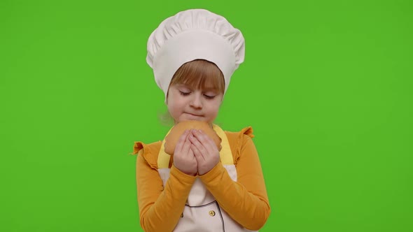 Child Girl 56 Years Old Dressed in Apron Like Chef Cook Eating Tasty Bun on Chroma Key Background