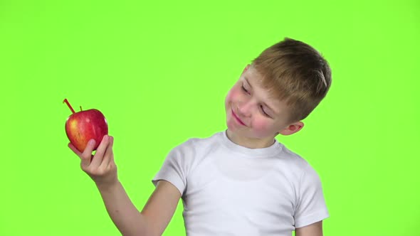 Little Boy Is an Apple with a Straw and Drinks Juice From It. Green Screen. Slow Motion