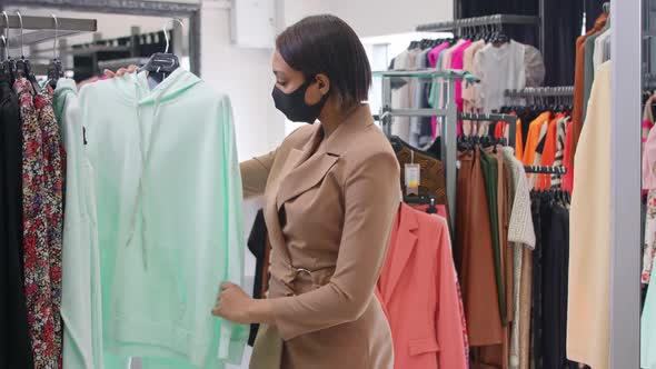 Fashionable African Woman in a Clothing Store Chooses a Tracksuit to Buy Woman in a Protective Mask