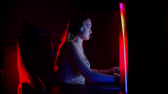 Sexy Tattooed Young Woman Sitting in Neon Gaming Club and Playing Game - Smiling and Looking in the