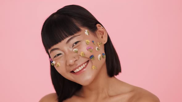 A happy asian woman posing to the camera with colorful flowers on her face