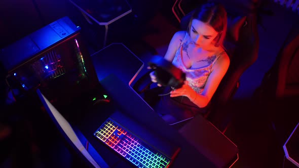 Young Attractive Gamer Woman Sits in the Chair in Neon Gaming Club and Playing Games