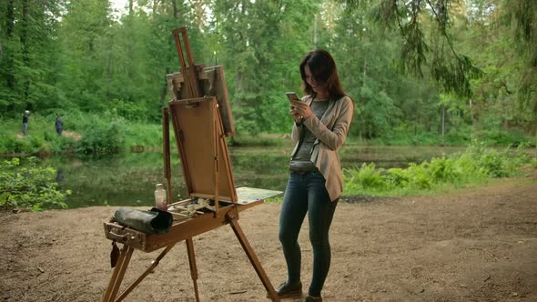 A Girl Artist, Next To an Easel and a Palette, Communicates with Her Friends on a Social Network