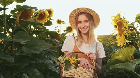 A Woman is Standing Through a Field of Sunflowers with a Basket of Flowers in Her Hands