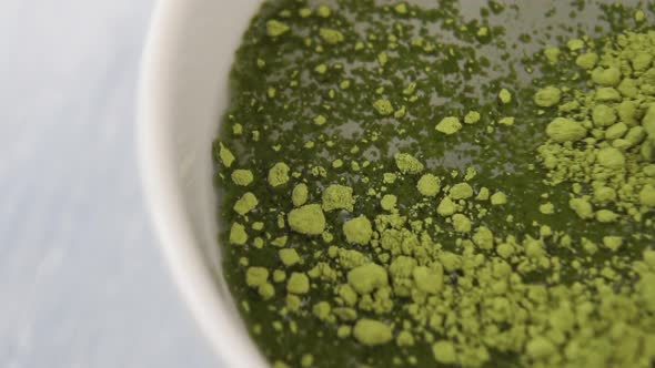 Matcha green tea is dissolved in boiling water in a white cup on a wooden surface close-up