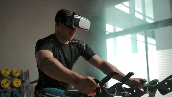 A Man Performs a Heavy Exercise on a Bicycle Simulator in a VR Helmet