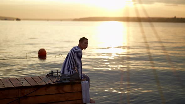 Sunrise Over Sea in Early Morning Young Man is Admiring Landscape Sitting on Wooden Pier