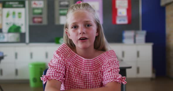 Portrait of causacian schoolgirl sitting at classroom, answering question, looking at camera