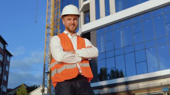 An Engineerarchitect in a White Shirt Helmet and Orange Work Vest Stands Against the Backdrop of a