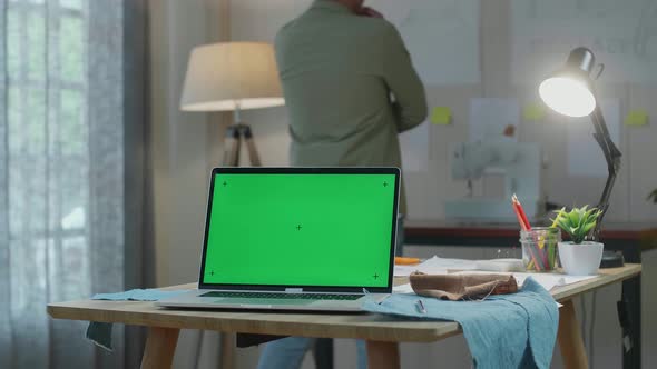 Green Screen Laptop Is On The Table While A Man Walks Into Looking At The Sketch Paper On The Wall