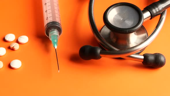 Close Up of Stethoscope, Pills and Syringe on Orange Background 