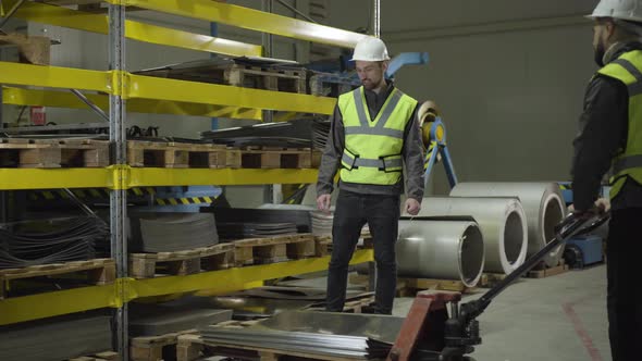 Worker Carrying Steel Metal Sheets with the Use of Trolley. Caucasian Man in Helmet and Vest