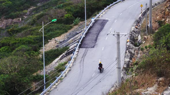 Tracking shot driving up a curvy road on motorbike carrying kite surfing board, watersports session