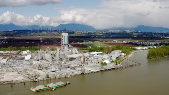 Sand Barge Sailing In The Fraser River With Cement Factory In Lulu Island, Richmond, BC, Canada. - a