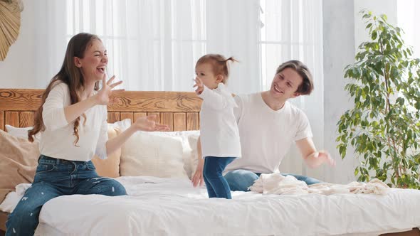 Family Having Fun at Home Bedroom in Morning Little Girl Toddler Dancing to Music on Bed Father and