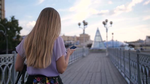 Back View of Blonde Woman Walking with Cellphone